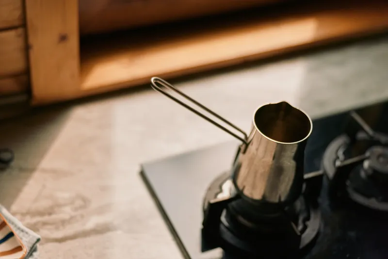 Closeup of a metal pot on a stove burner in a kitchen, highlighting cookware textures and a focused cooking scene with practical utensil details