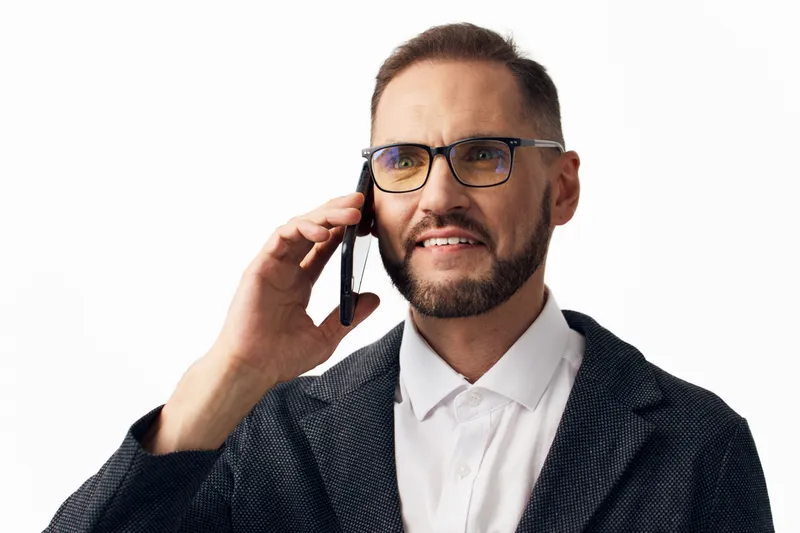 Professional businessman on a call stands against an isolated colored background, exuding focus and confidence with a thoughtful, composed expression.