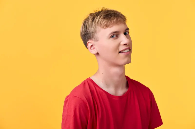 Man with a casual smile wearing a red shirt against a bright yellow backdrop, studio shot capturing a relaxed pose and confident style for fashion, lifestyle and marketing use