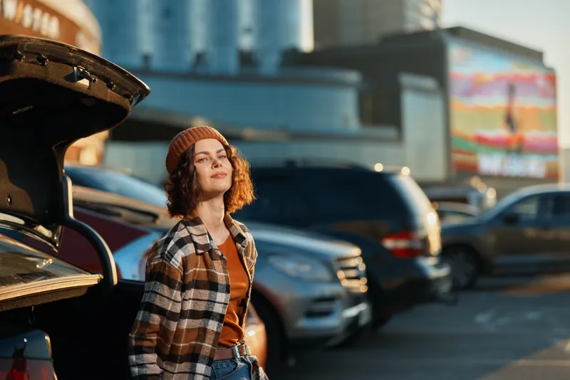 Woman with car in urban parking at golden hour, candid authenticity and mindful living captured in warm sunlight. Portrait of relaxed, confident youth and emotional storytelling.