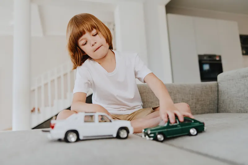 Young boy playing with toy cars in a cozy living room, engaging in imaginative play with his favorite vehicles while dressed in casual attire.
