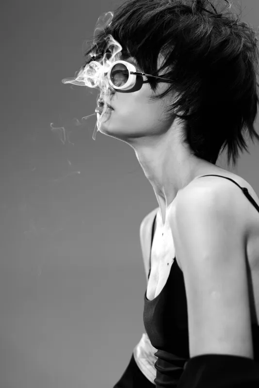 Black and white portrait of a young woman wearing sunglasses smoking with smoke curls around her face.