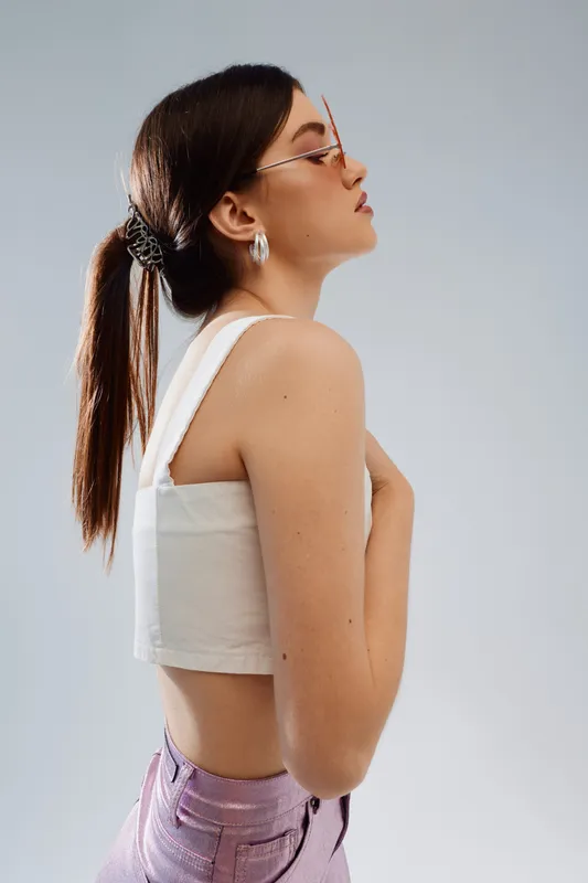 Young woman with long hair in a white top and pink pants poses sideways against a light background. Concept of beauty, fashion, style, and modern youth culture.