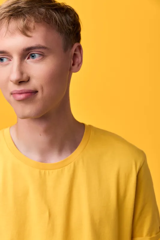 Youthful male model in a bright yellow shirt stands before a matching backdrop, conveying simple style and calm confidence, ideal for fashion, studio shoots and lifestyle branding campaigns
