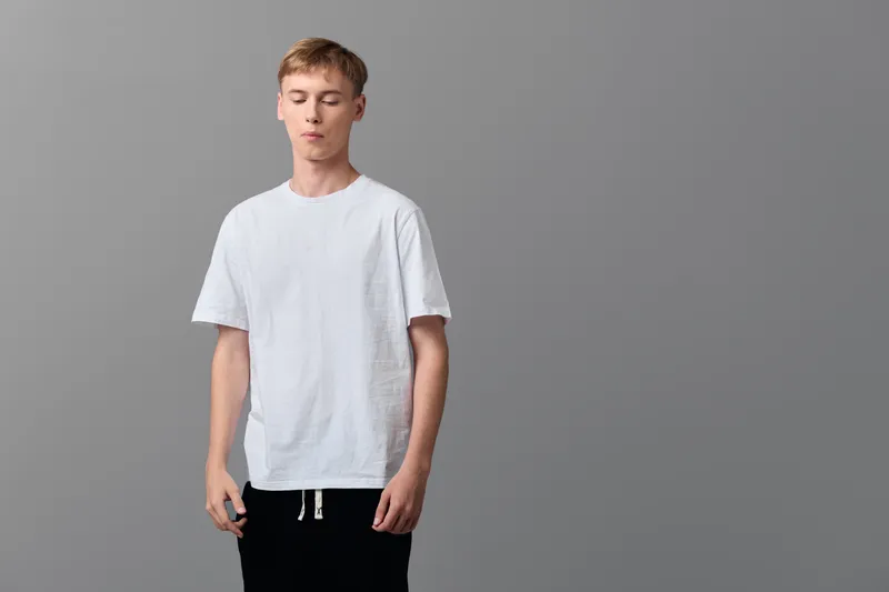 Casual man wearing a white t shirt stands in a simple studio with a relaxed pose, minimalist fashion vibe, and neutral gray backdrop
