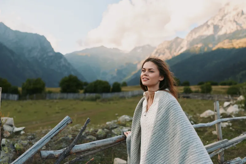 A woman in a light poncho stands in a mountain meadow, enjoying open sky and fresh air. A tranquil, nature inspired lifestyle moment.