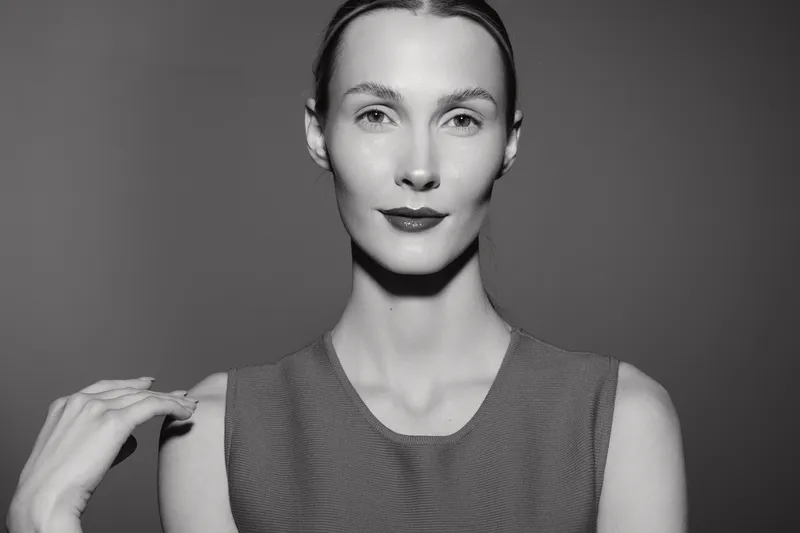 Portrait of a caucasian woman with light skin in a sleeveless top looking confidently at the camera. Minimalist studio lighting highlights her facial features and calm expression.
