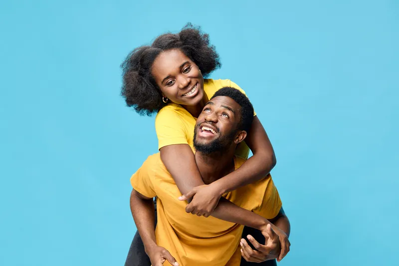 Happy African American couple smiling together in matching yellow shirts against a vibrant blue background, capturing joyful love and connection