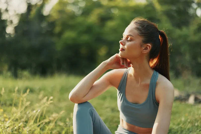 Young woman in athletic wear enjoying nature, exuding calmness and tranquility in a green outdoor setting during a sunny day