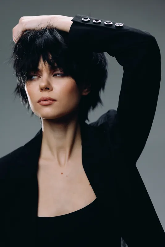 Stylish woman with short black hair posing in black jacket, modern fashion, confident expression, minimalistic background