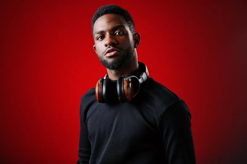 Stylish young Black male model wearing headphones with a confident expression against a vibrant red background, perfect for music and lifestyle themes