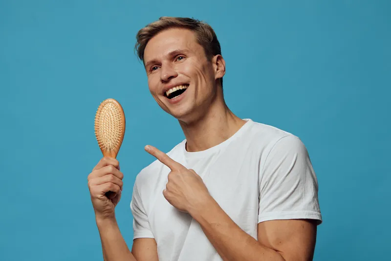 smiling man with hairbrush holding pointing white casual t-shirt blue background positive emotions happy lifestyle concept
