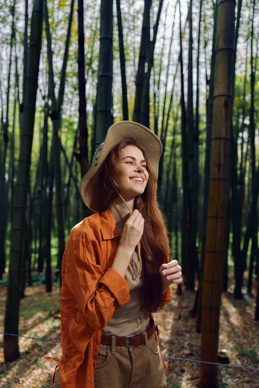 woman smile hat bamboo forest nature portrait, young redhead woman wearing a straw hat and orange jacket smiling in a tall bamboo grove, outdoor lifestyle travel and peaceful mood