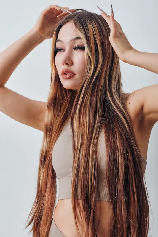 Woman with long straight hair and natural makeup posing with hands near head against plain background. Fashion model portrait with smooth skin and elegant hairstyle.