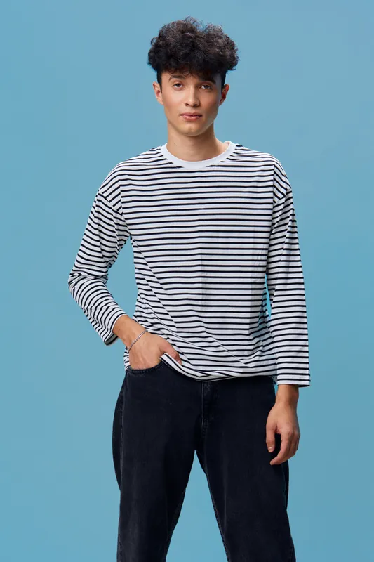 young man wearing striped shirt standing against blue background with casual posture and calm expression, modern style portrait in natural lighting