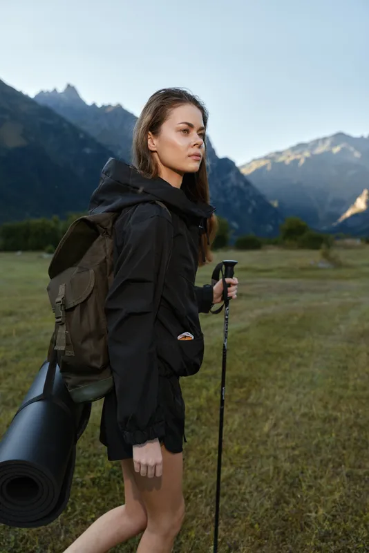 A focused solo hiker walks across a vast valley, carrying a backpack and a rolled mat while trekking through rugged outdoor scenery under clear skies.