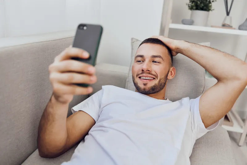 A smiling man enjoying a moment of relaxation, engaging with his smartphone. The scene reflects the balance between technology use and personal well-being.