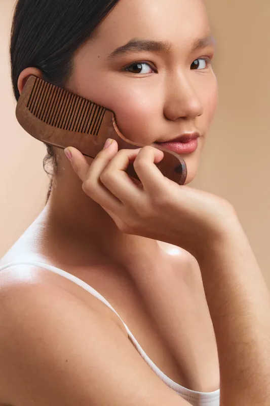 asian woman portrait closeup as she gently holds a wooden comb to her hair, serene expression, warm studio lighting, soft focus, calm beauty, poised and confident.