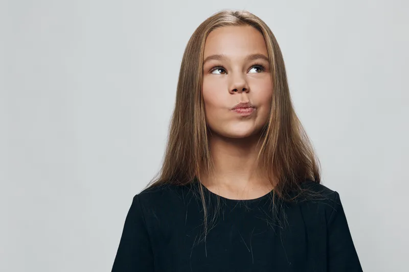 Girl with long hair in black shirt looking up and thinking on gray background. Female child with expression for ideas, curiosity, planning or wonder in studio portrait.