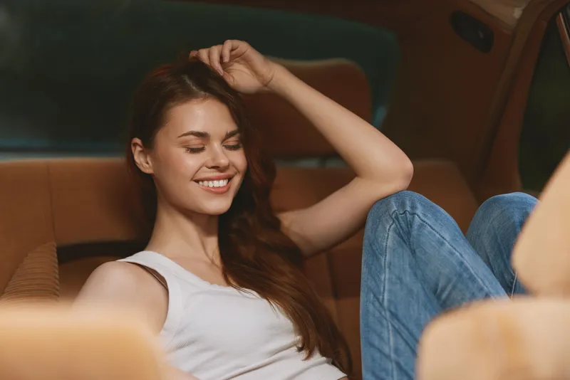 Relaxed young woman enjoying a moment of calm in a cozy car interior, wearing casual attire with a joyful expression, reflecting comfort and contentment.