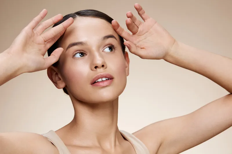 Young woman with natural beauty poses gracefully with soft lighting, highlighting her glowing skin, expressing serenity and confidence against a neutral background