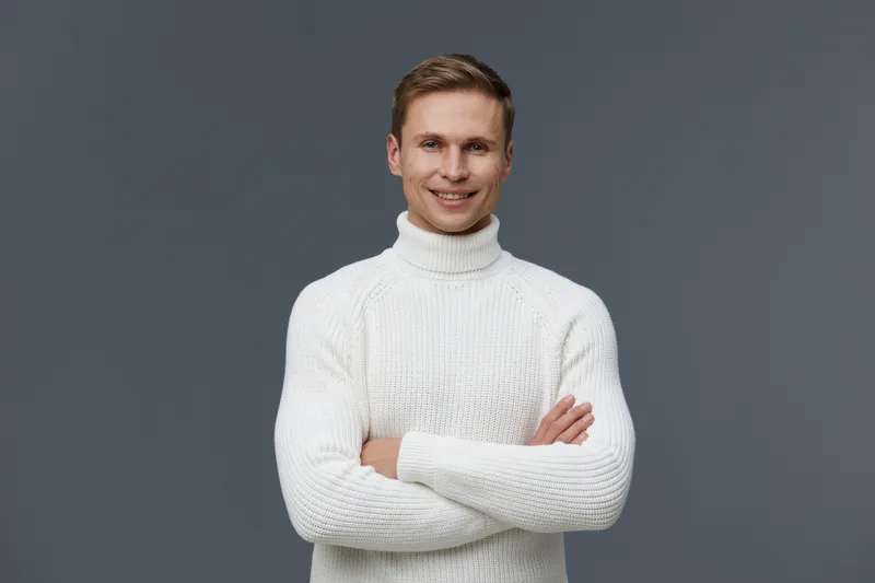 Smiling man wearing white turtleneck sweater looking at camera confident friendly pose isolated on gray background studio portrait. People lifestyle concept