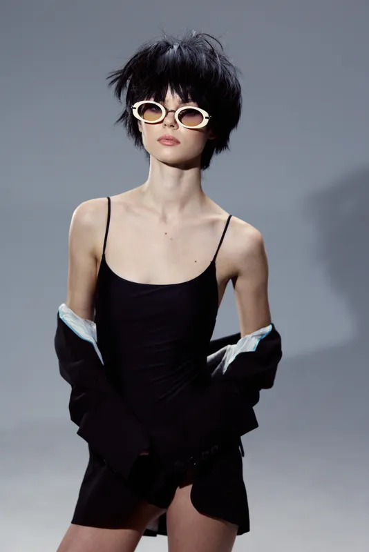 stylish woman in black dress wearing white sunglasses with edgy hairstyle and confident pose