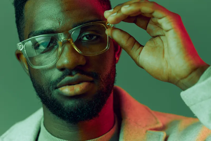 Stylish young man wearing glasses with colorful background, showcasing confidence and charisma in a modern fashion setting