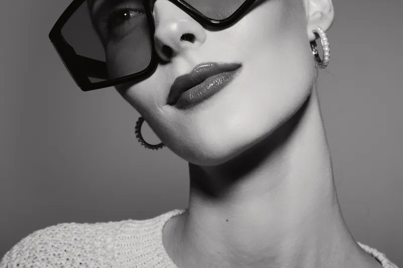 Stylish Caucasian woman with pale skin wearing large sunglasses and hoop earrings in black and white close-up portrait.