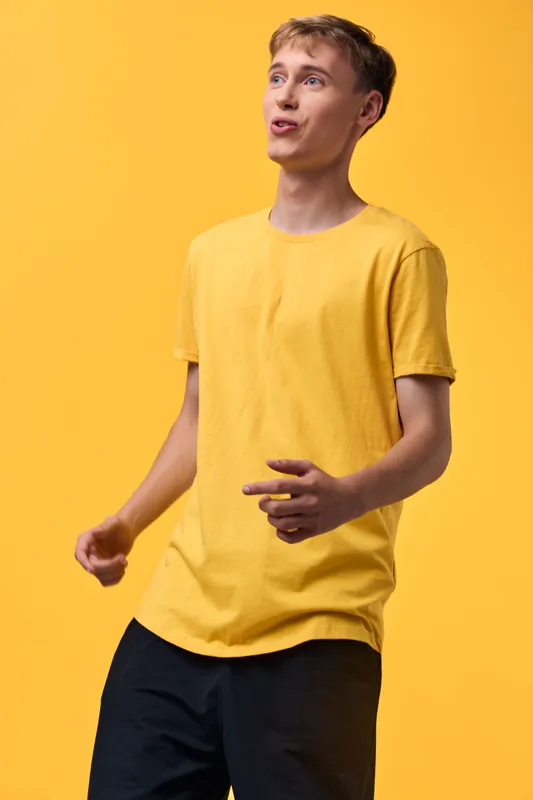 Man in a bright yellow t shirt poses with a playful expression against a yellow backdrop, capturing casual style, energy, and upbeat mood for lifestyle or fashion stock photo.