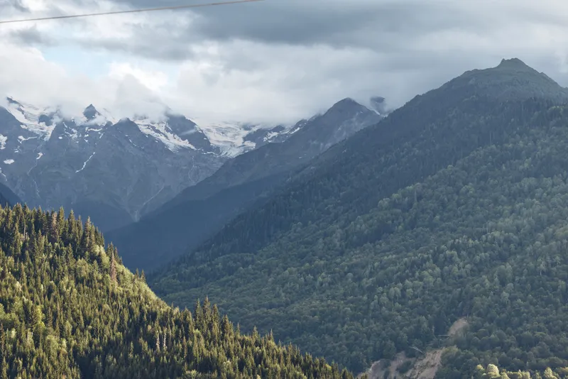 Mountain forest landscape with misty clouds and distant snow peaks, serene nature scene with layered ridges, evergreen trees and moody sky, authenticity inclusivity