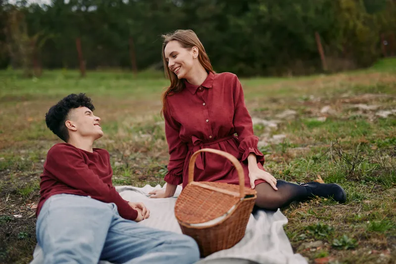 A genuine candid portrait of a young couple sharing a relaxed outdoor picnic on a blanket, natural smiles and authentic interaction conveying warmth, trust and believable everyday connection.