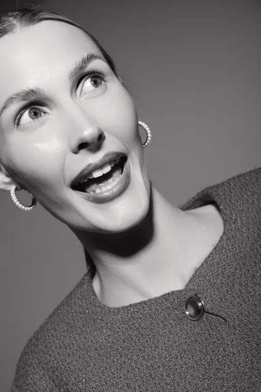 Surprised white woman with light skin looks aside wearing earrings and textured clothing. Black and white portrait with bright studio lighting and expressive emotion.