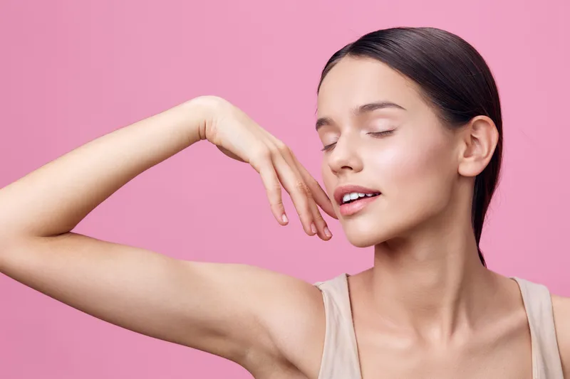 A serene young woman with fair skin showcasing natural beauty, dressed in a simple beige top against a soft pink background, expressing tranquility and confidence