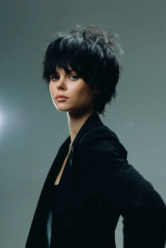young woman with short black hair wearing dark clothing against gray background
