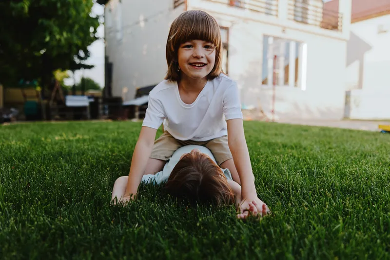 Happy children playing on green grass, enjoying their time outdoors in a sunny garden. Their laughter and joy create a lively atmosphere of childhood innocence.
