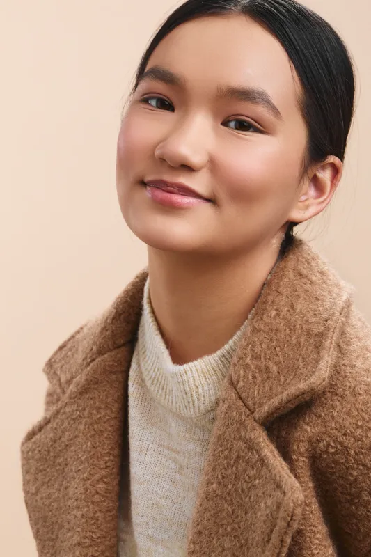 Asian woman portrait in soft studio light, wearing a beige knit coat and cream sweater, presenting a calm, confident vibe ideal for professional lifestyle imagery.