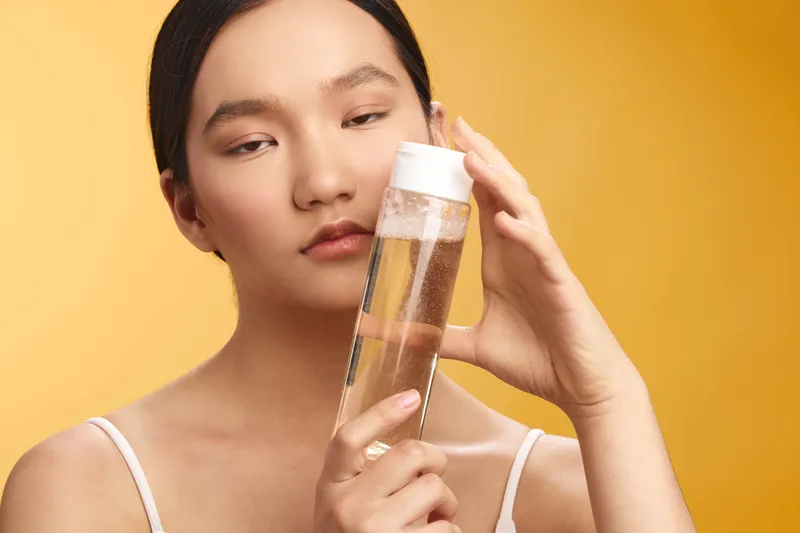 asian woman inspecting a clear glass test tube filled with liquid in a bright studio, conveying focus, curiosity, and a modern scientific vibe in a warm, inviting environment.