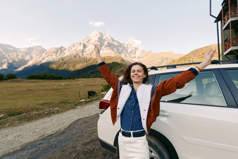 Woman car mountains nature travel road happy outdoors freedom smile portrait: smiling woman next to SUV on gravel road with arms raised, joyful travel portrait in scenic landscape and mountain