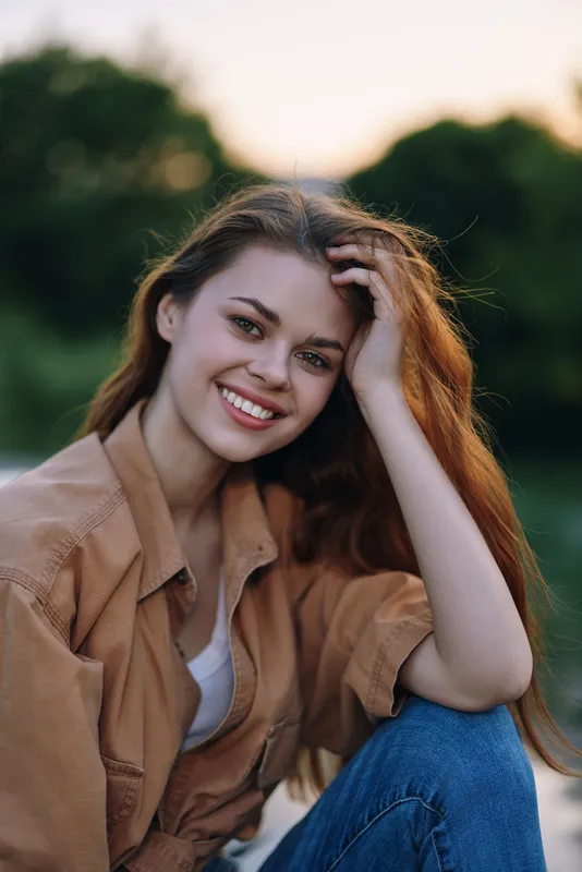 Young woman smiling outdoors in casual attire, with long hair, showcasing happiness and warmth, perfect for lifestyle and beauty concepts.