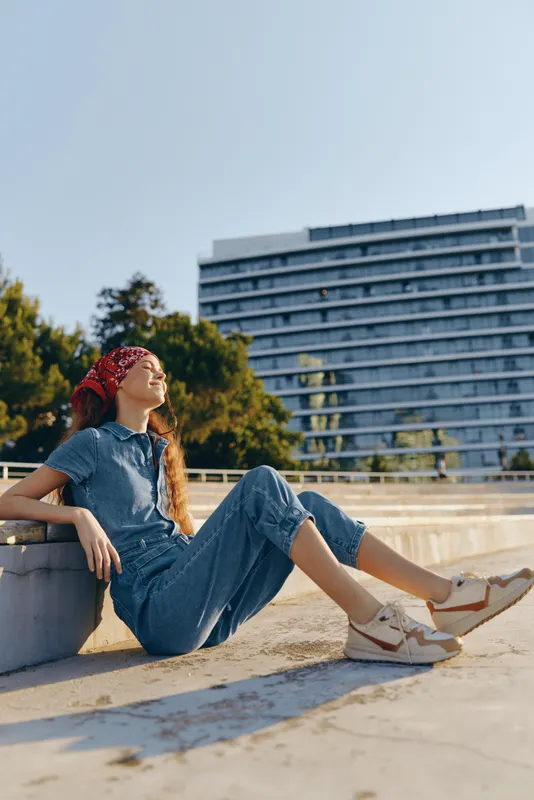 lifestyle woman in modern boho-western denim street style relaxing outdoors with film color effect under bright sunlight in urban environment