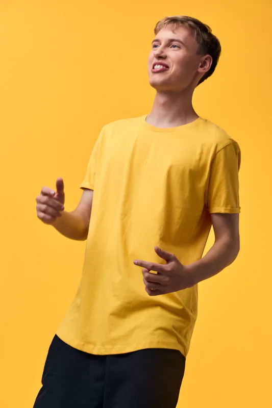 Cheerful man in a yellow shirt on a vibrant yellow backdrop, giving a thumbs up with a confident pose, conveying positivity, casual fashion, and everyday lifestyle for marketing and stock use