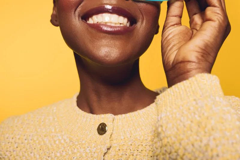 Close-up of smiling black woman with dark skin wearing yellow knitted sweater on yellow background. Concept of happiness, joy, fashion, and positive emotions in studio lighting.