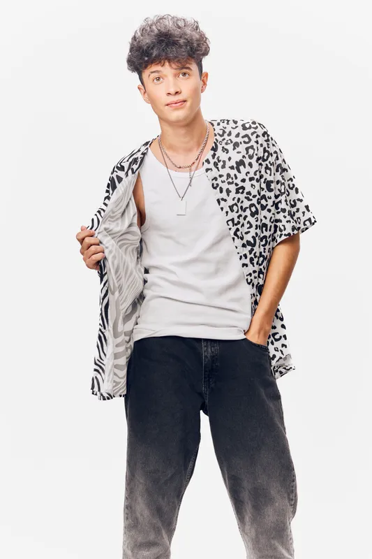 young man wearing leopard print shirt and white tank top poses confidently with hand in pocket, styled with black jeans, casual fashion on white background