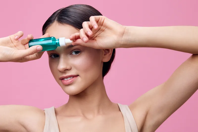 Young woman showcasing a beauty serum against a pink background, expressing confidence and excitement, emphasizing skincare and self care