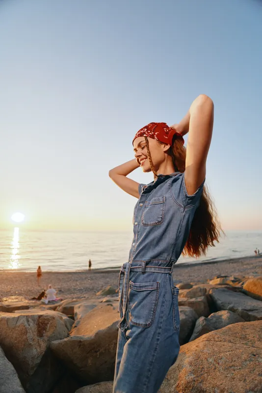 lifestyle woman in modern boho-western denim street style with a red bandana by the beach at sunset, film color captures relaxed summer mood