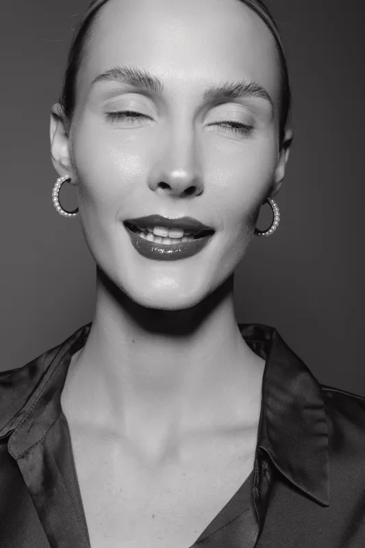 Close-up of a smiling Caucasian woman with fair skin and sleek hair wearing hoop earrings and a dark shirt. Concept for beauty, fashion, and positive emotion in studio lighting.