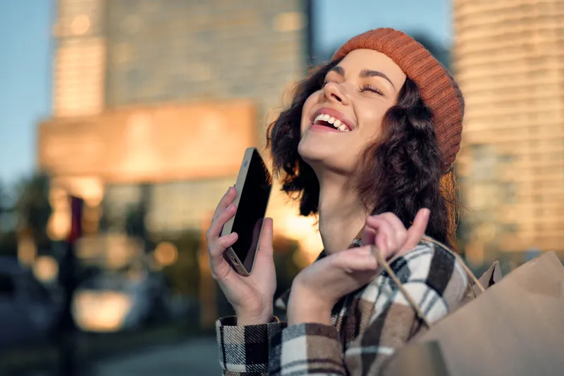 woman portrait smiling in urban streets at golden hour, holding phone and shopping bag in candid lifestyle scene with authenticity, mindful living and emotional storytelling warmth