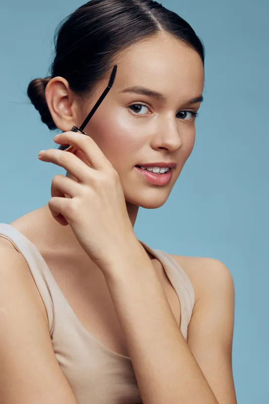 Young woman with natural makeup holding eyebrow brush, showcasing clear skin and confident expression, perfect for beauty and skincare concepts