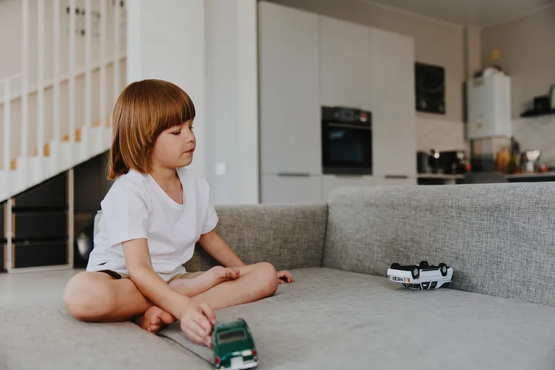 Young boy playing with toy cars on a cozy sofa in a modern living room, showcasing focus and imagination, surrounded by a warm and inviting atmosphere.